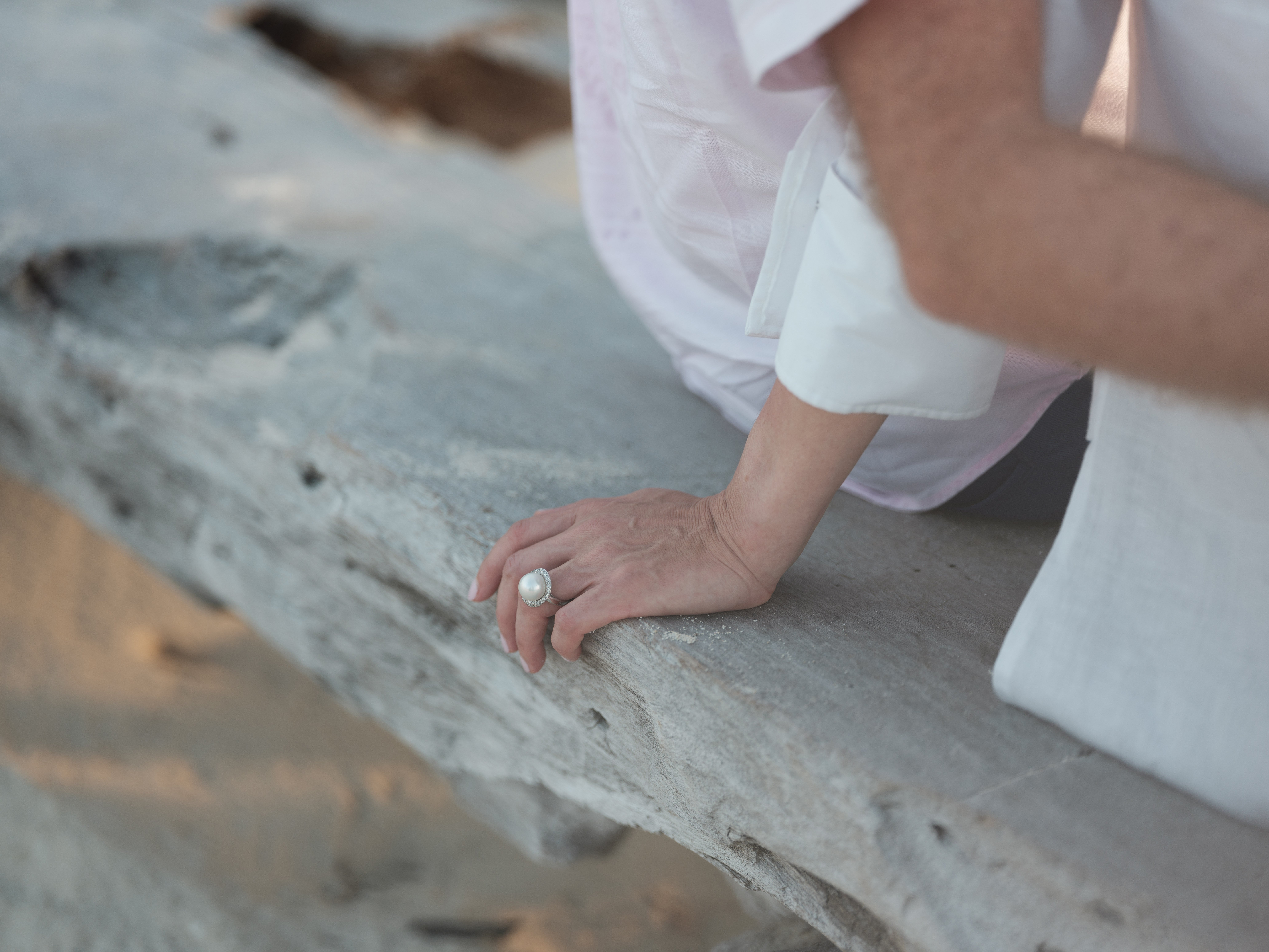 couple_sitting_woman_hand_pearl_ring_resting_on_beach_driftwood (3)