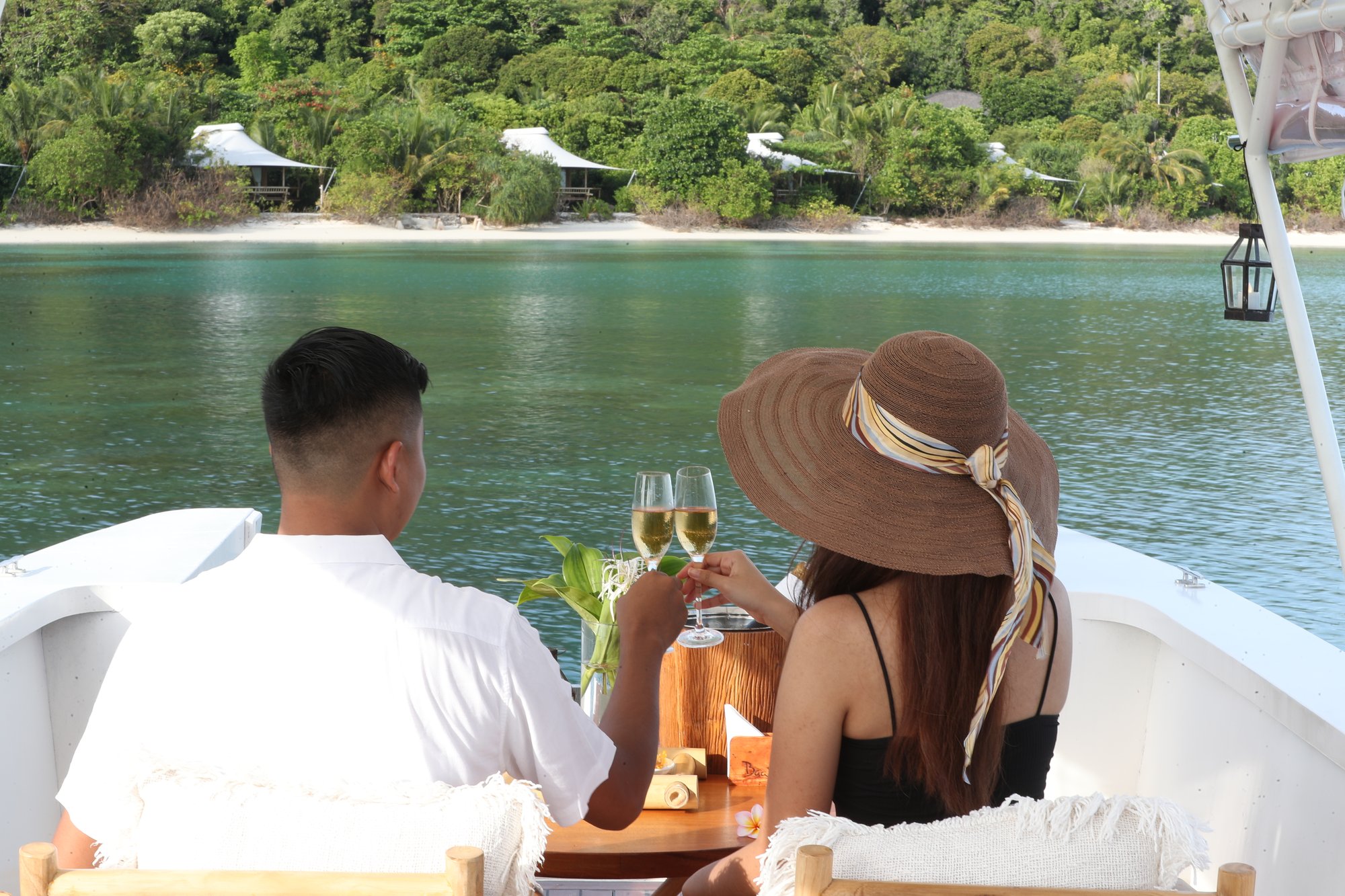 young-couple-male-white-top-female-straw-hat-black-tank-top-tossing-wine-on-sunset-cruise-boat-deck-looking-beach-suites-lagoon-raw