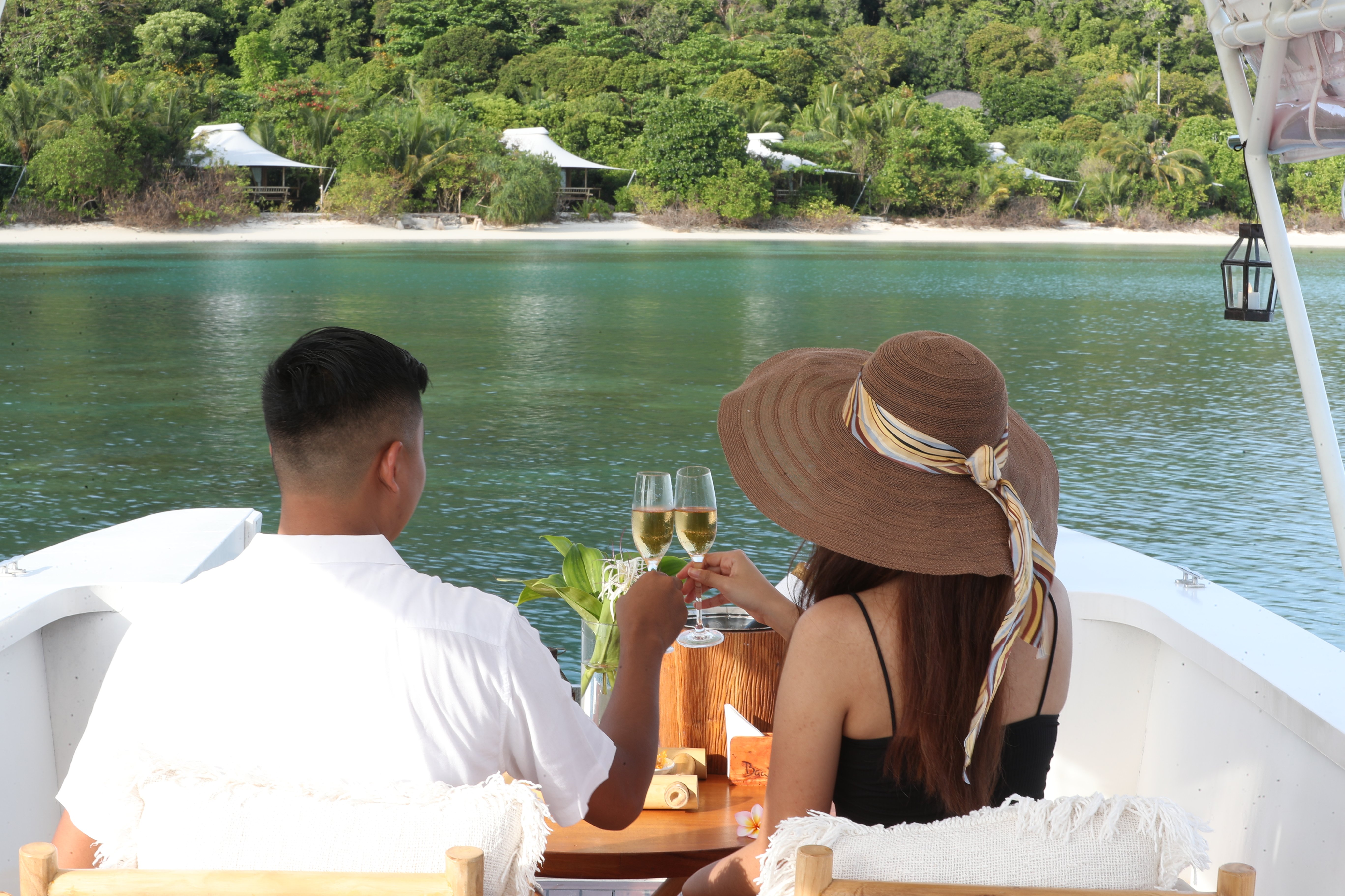 young-couple-male-white-top-female-straw-hat-black-tank-top-tossing-wine-on-sunset-cruise-boat-deck-looking-beach-suites-lagoon-raw