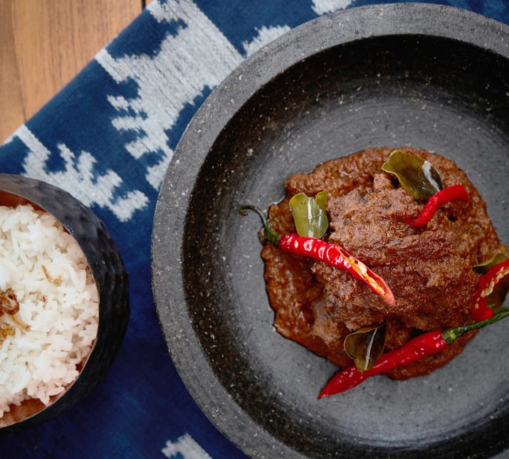 close_up_beef_rendang_on_stone_mortar_with_white_rice_on_ikat_cloth (1)