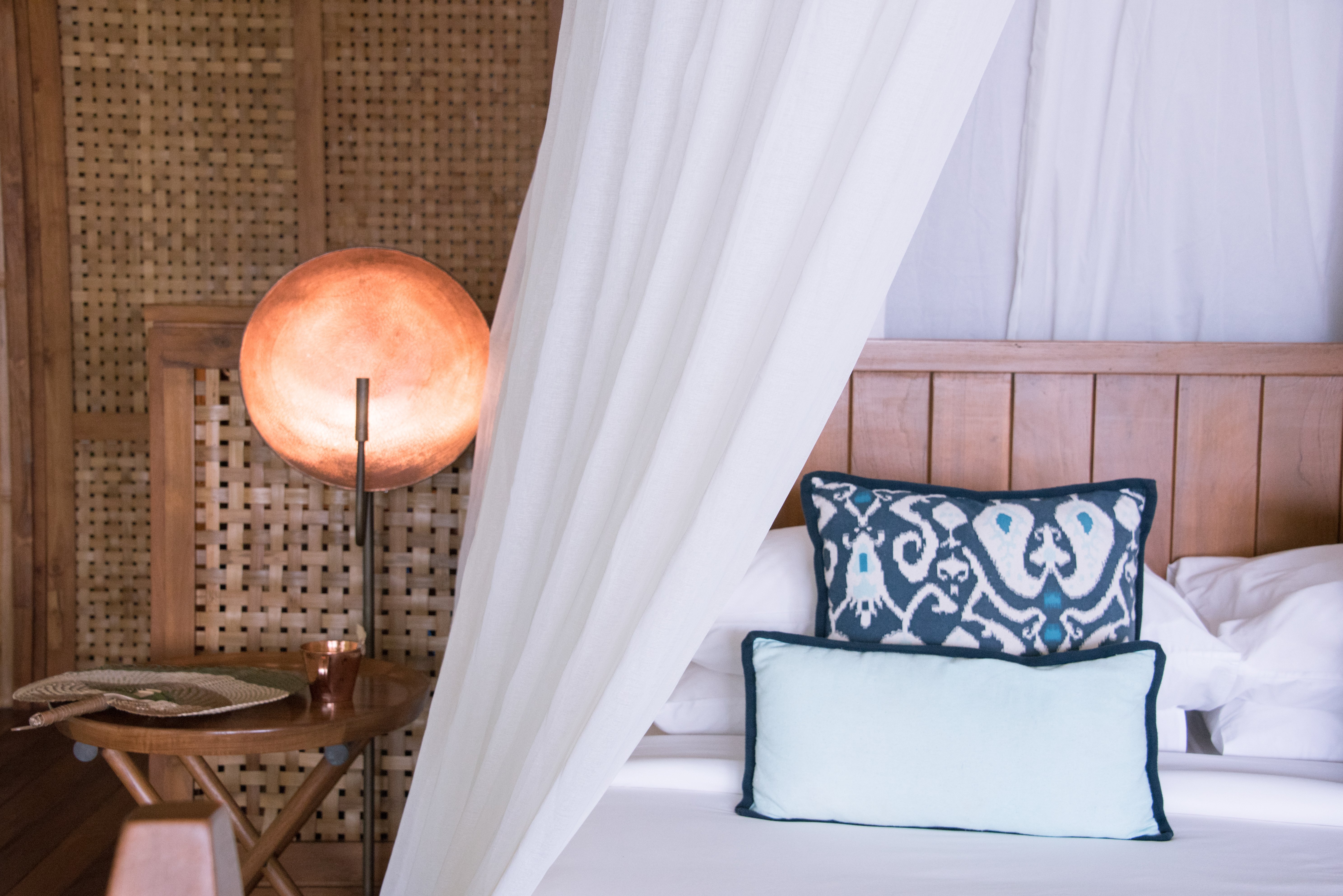 white_bed_canopy_with_cooper_bed_side_light_with_rattan_fan_on_table_beach_suite